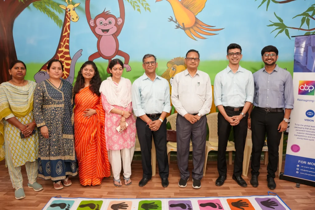 Group of people pose in front of a mural of zoo animals, with a mat displaying colorful hand and footprints on the floor.